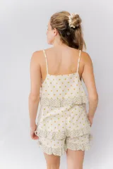 Pijama de algodón estampado con lunares dorados sobre fondo crema. Incluye una musculosa con tirantes finos y volados en el pecho, y un short con elástico en la cintura y volados en el ruedo. Los volados presentan un estampado floral en tonos verdes y crema.