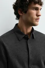 Camisa de corte relajado confeccionada en tejido de algodón con textura. Presenta cuello italiano, manga larga con puños abotonados y cierre frontal mediante botonadura.