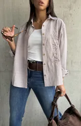 Camisa clásica a rayas verticales blancas y tostadas, con botones marrones y bordado floral en el frente.