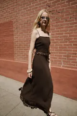 Falda midi pareo de color marrón, con diseño cruzado, cierre lateral con botón interior y lazada. Presenta detalles de bordados y flecos en el bajo.