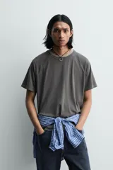 Camiseta relaxed fit color gris oscuro, confeccionada en tejido ligero de algodón con elasticidad. Presenta cuello redondo y manga ranglán corta.