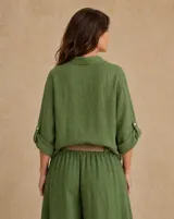 Camisa de lino verde oliva, de corte oversize y largo asimétrico, con cuello camisero, cierre frontal de botones, bolsillo aplicado en el pecho y mangas largas regulables con presilla.