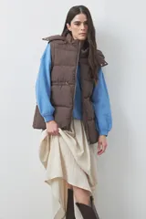 Chaleco puffer negro con diseño acolchado, capucha desmontable y cierre frontal. Cuenta con cordones ajustables en la cintura y bolsillos laterales.