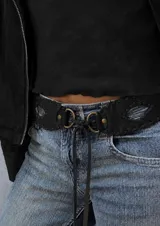 Cinto de cuero negro cosido a mano con detalles perforados, anillas metálicas doradas y tiras colgantes frontales.