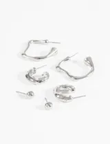 Set de tres pares de aros plateados con diseño irregular: un par de aros argolla con textura ondulada, un par de aros argolla pequeños con incrustaciones de perlas y strass, y un par de aros tipo botón con forma de esfera.
