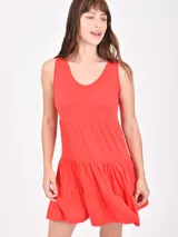 Vestido corto color coral, sin mangas, con escote en V y diseño de falda con volados escalonados.