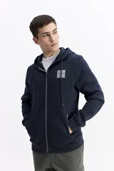 Campera con capucha de algodón y poliéster, color blanco, con cierre frontal negro y cordones negros en la capucha. Presenta un pequeño parche cuadrado negro con texto blanco en el pecho izquierdo y cierres negros en los bolsillos laterales.