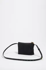 Bolso bandolera mini de Bimba y Lola en color negro, con cierre de cremallera superior, asas cortas de mano y tirador decorativo de cuerda con cuentas rojas. Presenta el logotipo de la marca impreso en letras doradas en la parte frontal.