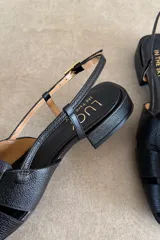 Sandalias de cuero color negro, estilo romanas con tiras entrelazadas en la parte delantera, talón descubierto y tira ajustable con hebilla metálica.