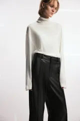 Pantalón de tiro alto efecto piel en color marrón, con pierna ancha y costuras marcadas en la parte delantera. Presenta trabillas en la cintura y cierre frontal con cremallera, botón y gancho metálico.