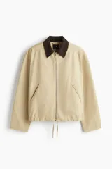 Campera tipo blouson de algodón color beige claro, con cuello de pana marrón oscuro. Posee cierre frontal, bolsillos delanteros ribeteados y elástico ajustable con cordón en el bajo.