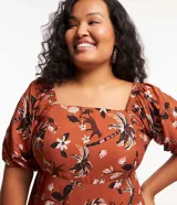 Vestido corto color ladrillo con estampado de flores y palmeras en tonos blanco y negro. Tiene escote cuadrado, mangas cortas abullonadas y falda con volantes.