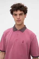 Remera polo de manga corta color rojo con efecto lavado, cuello y puños en contraste marrón. Cuenta con media cartera de botones, aberturas laterales en el dobladillo y un bordado pequeño de una estrella en el pecho.