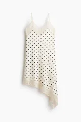 Vestido midi de satén blanco con estampado de lunares negros, escote en V con ribetes de encaje, breteles finos y bajo asimétrico con detalles de encaje.