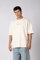 Remerón de corte oversized confeccionado en tejido rústico, con cuello redondo y mangas cortas. Presenta un diseño minimalista con una pequeña estampa frontal centrada en el pecho.