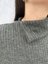 Polera de punto acanalado en color verde oliva, con cuello alto abierto lateralmente y mangas largas amplias. Presenta un diseño de corte recto y holgado.