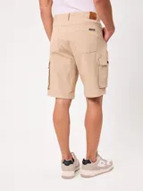 Bermuda cargo de gabardina color beige, con bolsillos laterales con fuelle en las piernas, bolsillos delanteros tipo ojal y traseros. Cuenta con presillas para cinto y cierre frontal con botón y cierre.