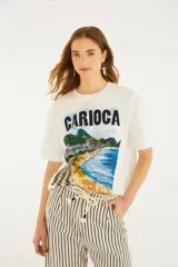 Remera blanca de manga corta y cuello redondo, con estampa frontal ilustrada de un paisaje de playa con la inscripción "Carioca".