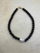 Collar artesanal compuesto por cuentas de piedra volcánica en diversos tonos y tamaños, con una perla natural de río como dije central y cierre metálico dorado.