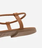 Sandalia plana de mujer color dorado metalizado, con diseño minimalista de tira fina que une la puntera y el empeine, y tira elástica fina alrededor del tobillo.