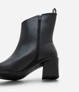 Bota corta de cuero sintético negro con diseño asimétrico en la caña, punta fina, taco bloque mediano y tirador trasero.