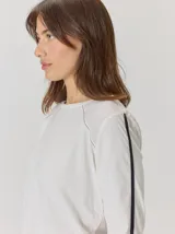 Remera de manga larga color blanco con costuras decorativas en contraste y una franja lateral oscura en las mangas. Presenta un diseño de corte holgado y cuello redondo.