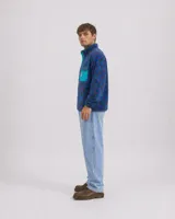 Buzo de polar fleece con diseño estampado geométrico en tonos azules, bordó y verde. Presenta cuello alto con cierre de botones a presión, bolsillo frontal con solapa en contraste y puños elásticos.