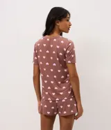 Pijama corto de dos piezas compuesto por una remera de manga corta con cuello redondo y bolsillo frontal, y un short de cintura elastizada. Ambos presentan un diseño estampado de corazones sobre fondo marrón.