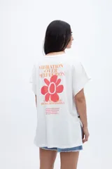 Musculosa blanca de algodón lavado con textura extra suave, calce oversize, mangas diferenciadas y tajos laterales. Presenta un estampado en la espalda con la frase "VIBRATION OVER PERFECTION" en naranja, una flor roja y texto adicional en naranja.