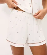 Pijama corto de dos piezas confeccionado en viscolycra blanca con estampado floral y vivo en contraste. Incluye una camisa de manga corta con cuello solapa y cierre frontal de botones, y un short con cintura elástica.