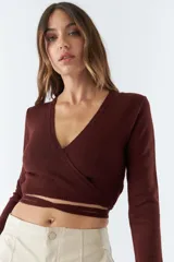 Top tejido de punto con diseño cruzado, escote en V y mangas largas. Cuenta con tiras para anudar en la cintura y detalle de grifa de cuero.