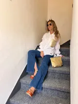 Camisa de brodery blanca de corte amplio, con cuello camisero, mangas largas con puños fruncidos y bolsillo frontal de cuero sintético metalizado dorado.
