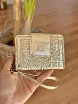 Billetera de cuero dorada con textura croco, cierre con broche y correa de muñeca.