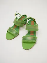 Sandalias de taco redondo de 6 cm, confeccionadas en gamuza verde con tiras frontales y de tobillo en material translúcido. Cuentan con cierre de pulsera al tobillo y plantilla de cuero.
