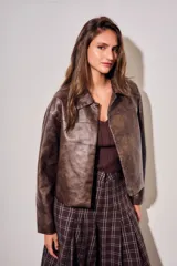 Campera de cuero vegano en tono marrón con acabado desgastado, corte recto y cierre frontal con botones a presión. Presenta cuello clásico y diseño minimalista.