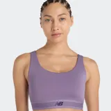 Top deportivo New Balance de impacto moderado, color violeta, con diseño de cuello redondo y banda elástica inferior con logo de la marca. Incluye copas extraíbles.