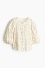 Blusa en tejido liviano de mezcla de lino, de color blanco con estampado floreado. Cuenta con cuello redondo, cierre frontal de botones y mangas globo tres cuartos con puños elásticos.