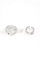 Set de dos anillos plateados de estilo moderno. Uno es un anillo abierto con diseño orgánico y texturizado, y el otro es un anillo abierto con bandas cruzadas que simulan un nudo o trenzado.
