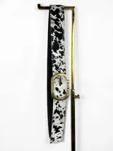 Cinto de cuero de pelo con estampado animal print tipo vaca en color blanco y negro, con hebilla metálica ovalada en tono bronce viejo con la marca grabada.