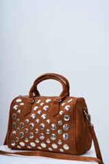 Bolso tipo bowling de gamuza color marrón con tachas plateadas. Tiene doble asa corta y correa larga desmontable.