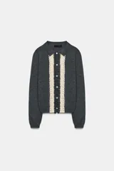 Chaqueta de punto gris oscuro con cuello solapa y manga larga. Presenta un diseño frontal con detalle de puntilla en color crema a contraste y cierre con botones.