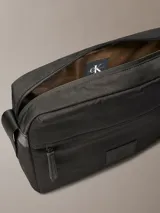 Bolso bandolera Calvin Klein color negro, confeccionado en nylon reciclado, con cierre de cremallera, asa superior y correa ajustable. Presenta un bolsillo frontal con cremallera y parche con el monograma CK en la parte delantera.