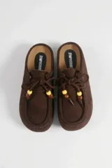 Mocasín destalonado de gamuza color marrón, con diseño tipo zueco, costuras pespunteadas en el empeine, cordones frontales decorados con cuentas y suela plana de goma.
