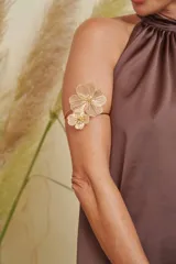 Brazalete dorado con diseño de dos flores de hibisco caladas, con detalles de pedrería en el centro.