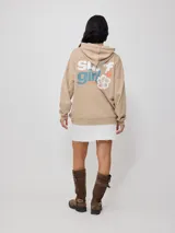 Canguro con capucha y bolsillo tipo canguro, color beige, con estampado frontal y elástico en puños y cintura.