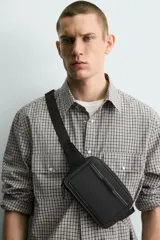 Riñonera negra con textura grabada, compartimento principal con cierre de cremallera y bolsillo frontal plano. Incluye asa ajustable con hebilla metálica de liberación rápida.