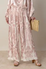 Pantalon palazzo de corte amplio y fluido, confeccionado en tela plisada con estampado estilo paisley en tonos beige y rosado. Presenta cintura elastizada y un diseño ligero ideal para climas cálidos.
