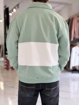 Buzo de algodón negro con una franja horizontal blanca en el centro, cuello solapa con medio cierre y puños y cintura elásticos acanalados. Cuenta con pequeños estampados en el pecho.