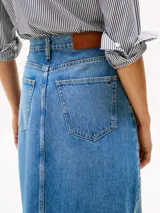 Falda midi de denim rígido celeste, corte recto de talle alto, con cinco bolsillos, abertura frontal y cierre de cremallera con botón.