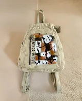 Mochila de cuero color natural con diseño pintado a mano de Carolina De Cunto, cuenta con un bolsillo frontal con cierre vertical y herrajes de metal.